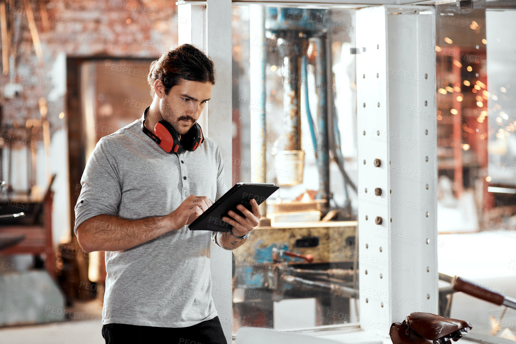 Buy stock photo Cropped shot of a handsome young businessman using a digital tablet in an office inside his workshop