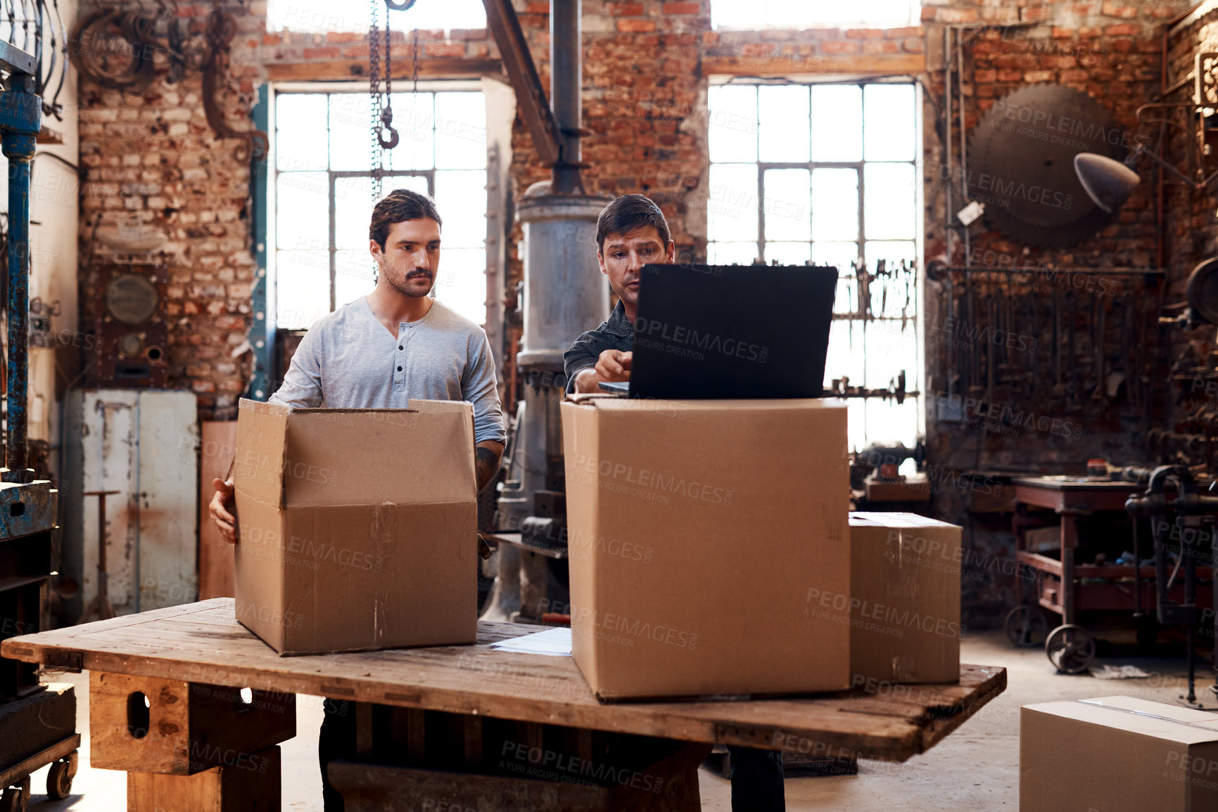 Buy stock photo Cropped shot of two young businessmen using a laptop while sorting out orders and deliveries inside their workshop