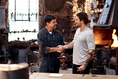 Buy stock photo Cropped shot of two handsome young businessmen shaking hands while working together inside a workshop