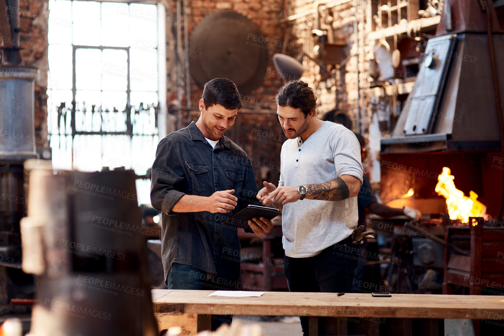 Buy stock photo Cropped shot of two handsome young using a digital tablet while working together inside their workshop