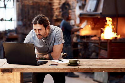 Buy stock photo Cropped shot of a handsome young businessman working on a laptop inside his workshop