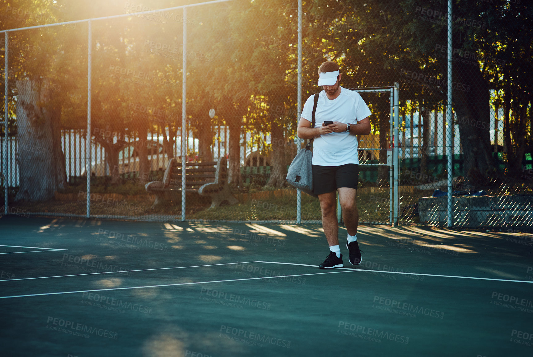 Buy stock photo Shot of a sporty young man using a cellphone while walking on a tennis court