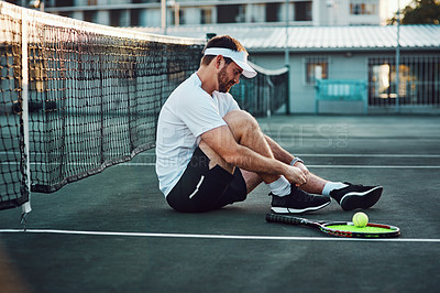 Buy stock photo Shot of a sporty young man tying his laces on a tennis court