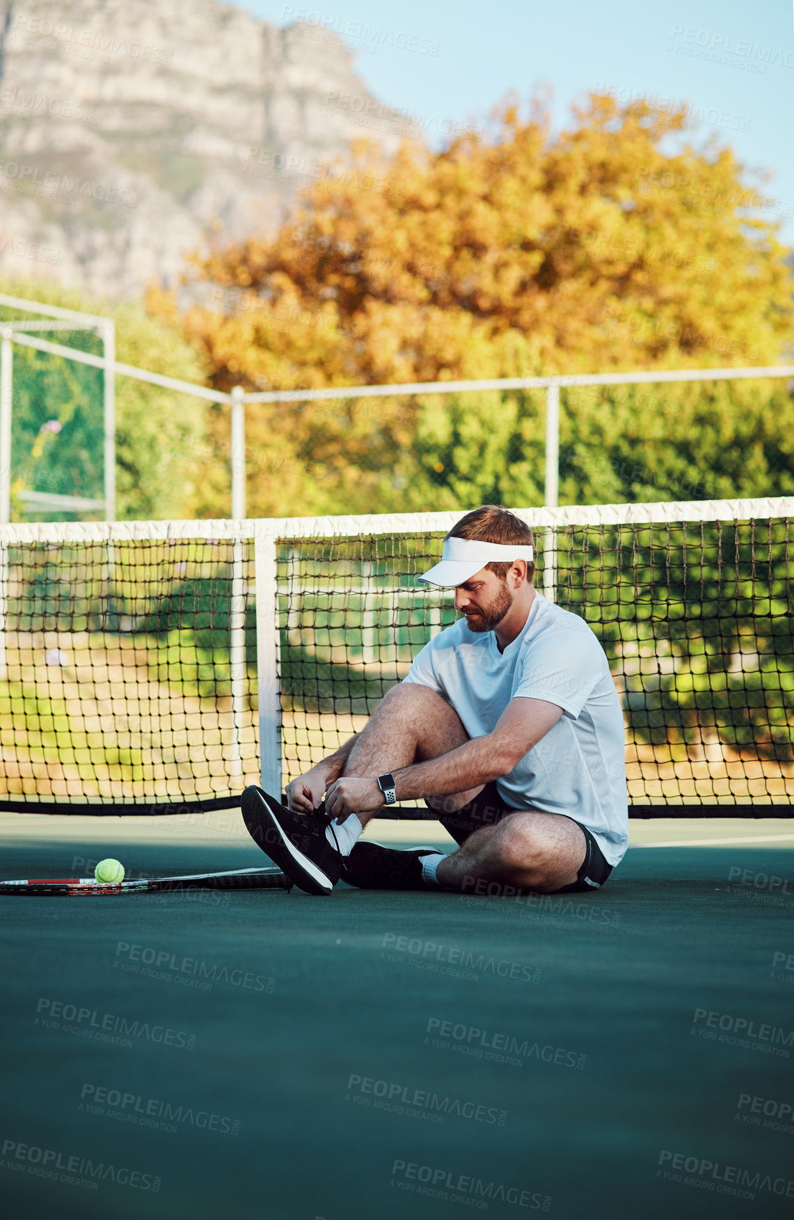 Buy stock photo Shot of a sporty young man tying his laces on a tennis court