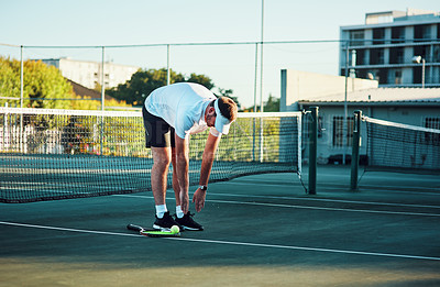 Buy stock photo Shot of a sporty young man touching his toes while stretching on a tennis court