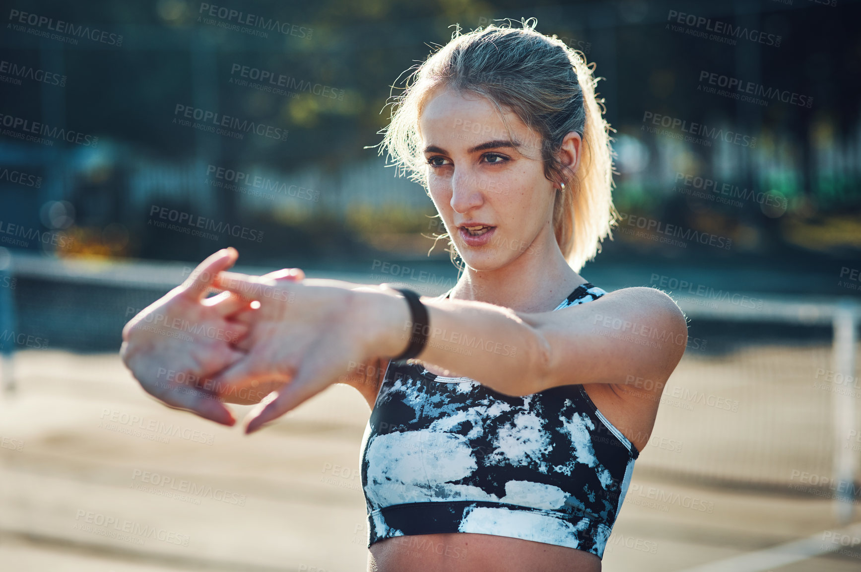 Buy stock photo Shot of a sporty young woman stretching her arms while exercising on a tennis court