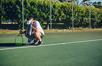 Buy stock photo Shot of a sporty young man wiping his face with a towel while playing tennis on a tennis court
