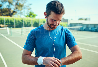 Buy stock photo Shot of a sporty young man checking his watch while exercising on a tennis court
