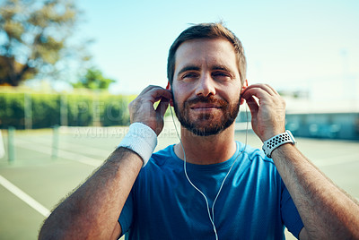 Buy stock photo Shot of a sporty young man listening to music while exercising on a tennis court