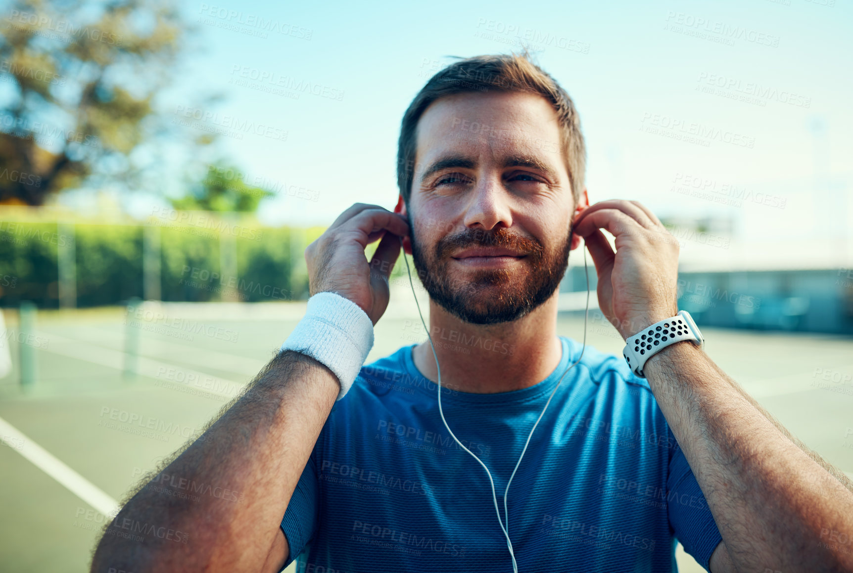 Buy stock photo Shot of a sporty young man listening to music while exercising on a tennis court