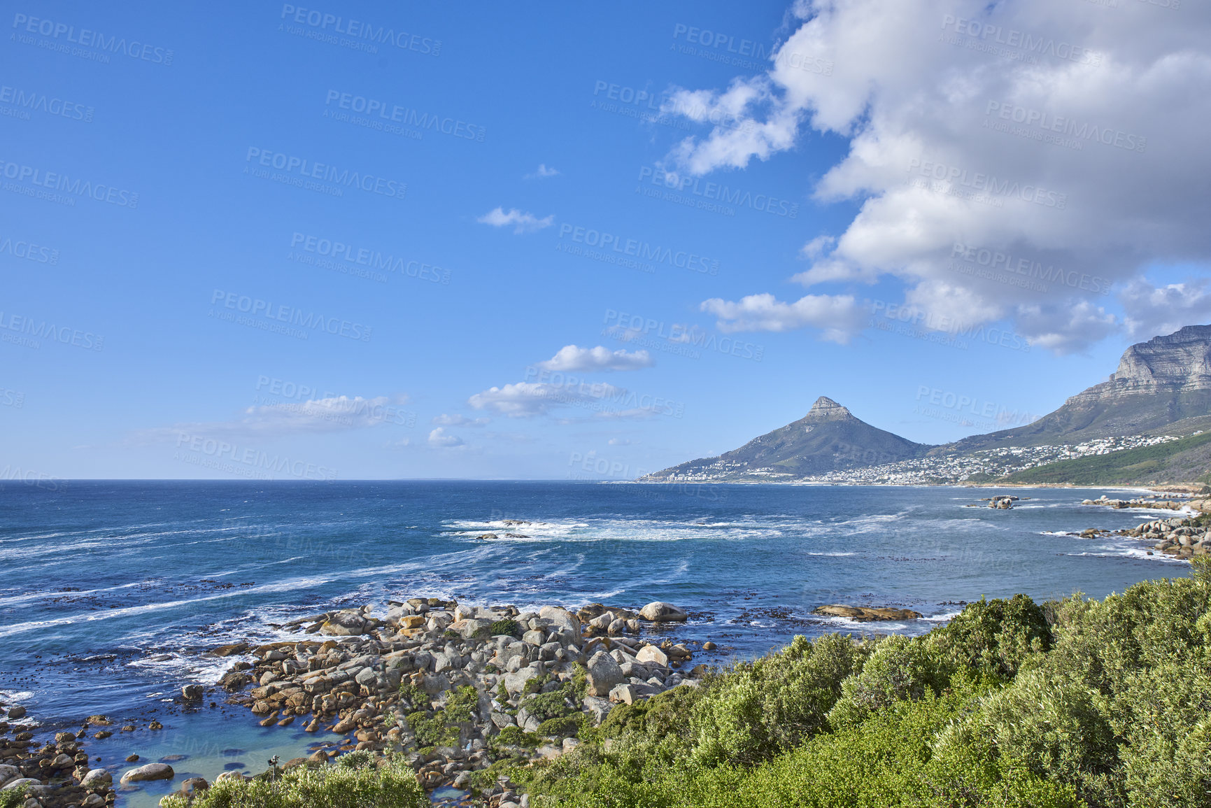 Buy stock photo A nature scenery of a calm sea and green bushes, with Lions Head mountain in the horizon, Cape Town, South Africa. Landscape of the ocean near the mountains with blue cloud sky and copy space.