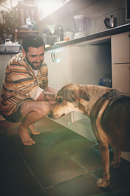 Buy stock photo Cropped shot of a cheerful young man calling his dog to eat his food inside of the kitchen during the da