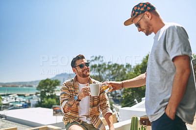 Buy stock photo Cropped shot of two cheerful young men enjoying a cup of coffee together outside on their balcony at home during the day