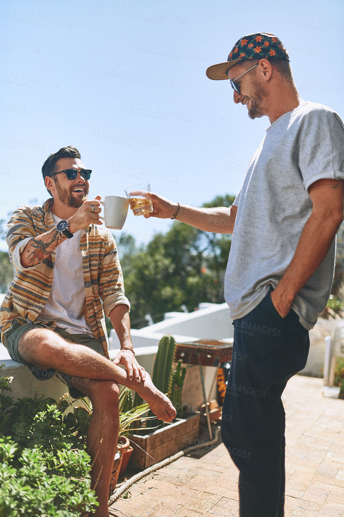 Buy stock photo Cropped shot of two cheerful young men enjoying a cup of coffee together outside on their balcony at home during the day
