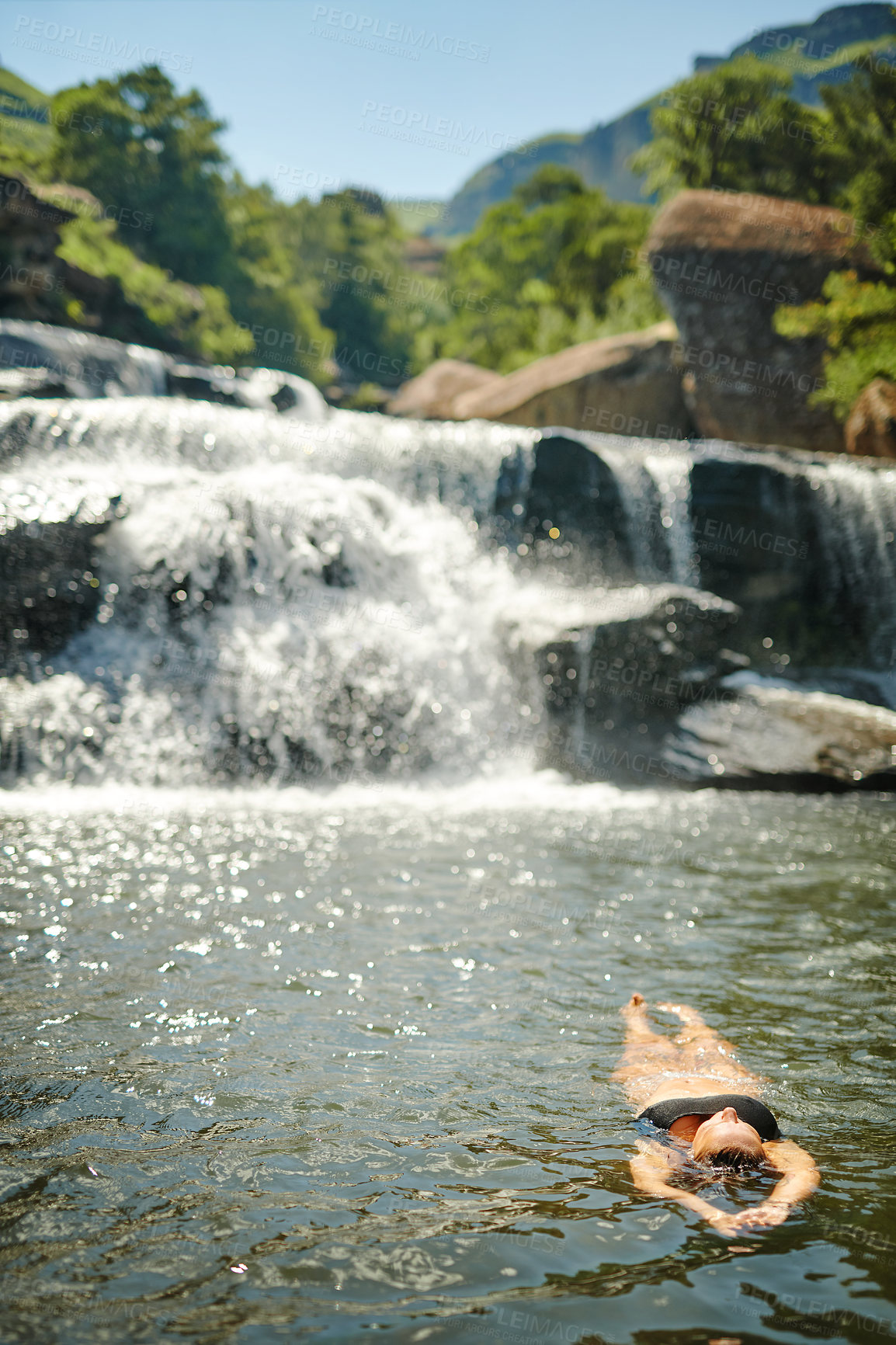 Buy stock photo Waterfall, mountain and woman float in river for adventure at travel destination, nature and outdoors. Weekend, journey and person relax in water, dam and stream for holiday, vacation and swimming