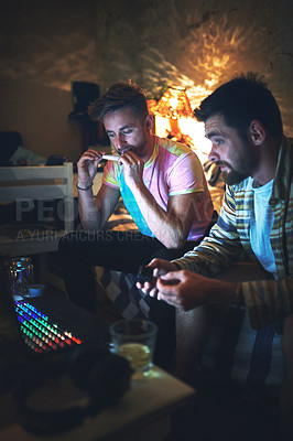 Buy stock photo Cropped shot of a handsome young man rolling a joint of cannabis while sitting with his friend at home