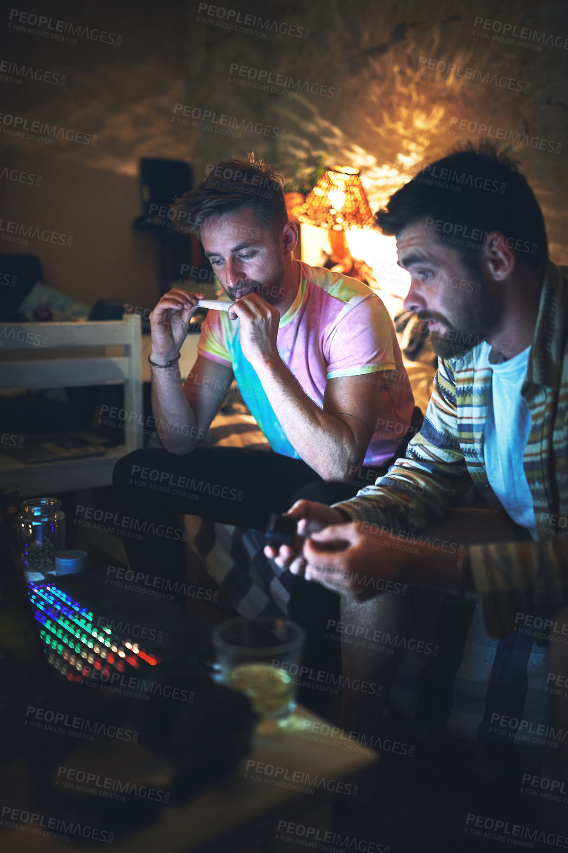 Buy stock photo Cropped shot of a handsome young man rolling a joint of cannabis while sitting with his friend at home