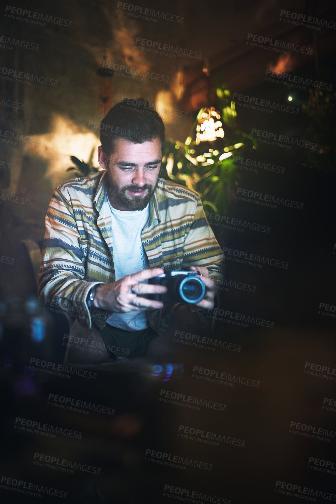 Buy stock photo Cropped shot of a handsome young man holding a camera while sitting indoors at home
