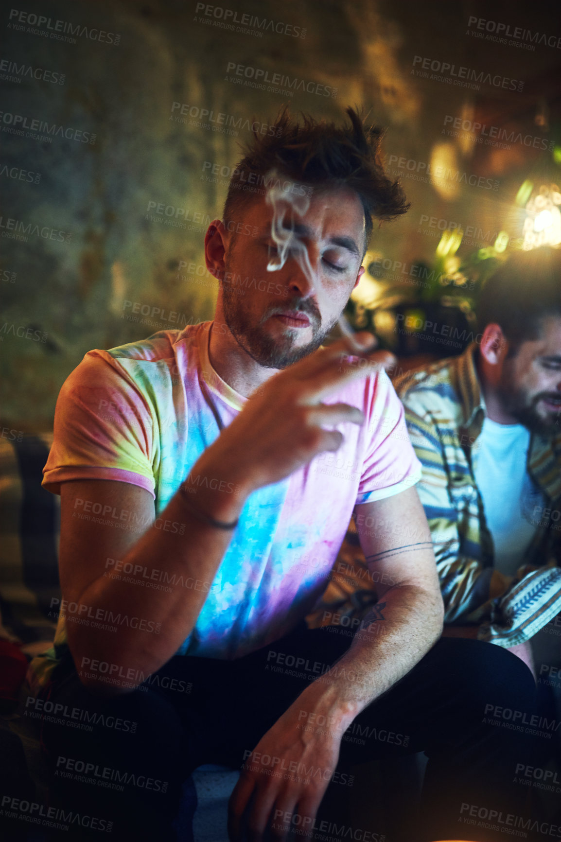 Buy stock photo Cropped shot of a handsome young man smoking cannabis while sitting with his friend at home
