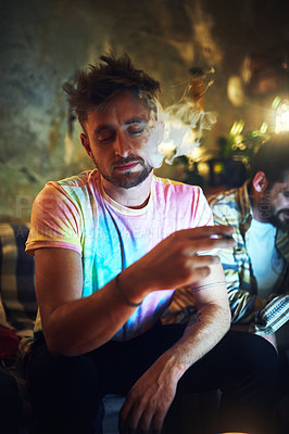 Buy stock photo Cropped shot of a handsome young man smoking cannabis while sitting with his friend at home