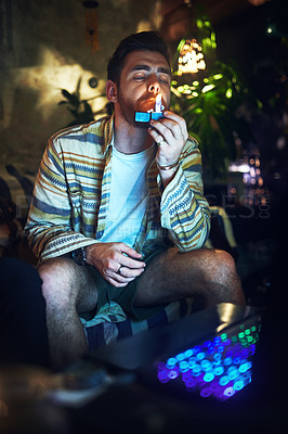Buy stock photo Cropped shot of a handsome young man lighting up a joint of cannabis at home