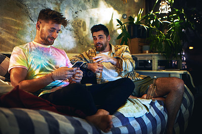 Buy stock photo Cropped shot of a handsome young man using a smartphone while sitting with his friend at home