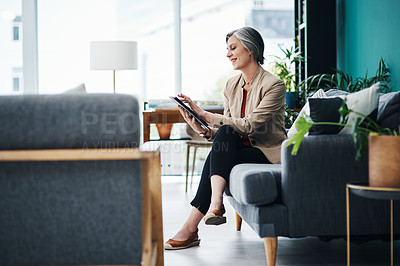 Buy stock photo Full length shot of an attractive mature businesswoman sitting alone and using a tablet in her home office