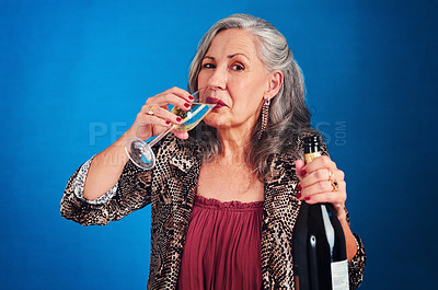Buy stock photo Portrait of a funky and cheerful senior woman drinking champagne in studio against a blue background
