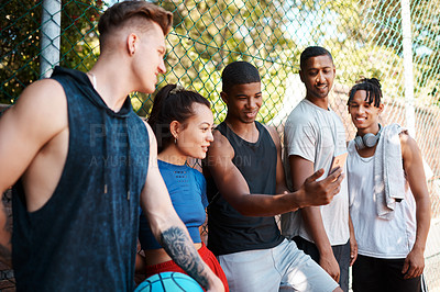 Buy stock photo Shot of a group of sporty young people looking at something on a cellphone while standing along a fence outdoors