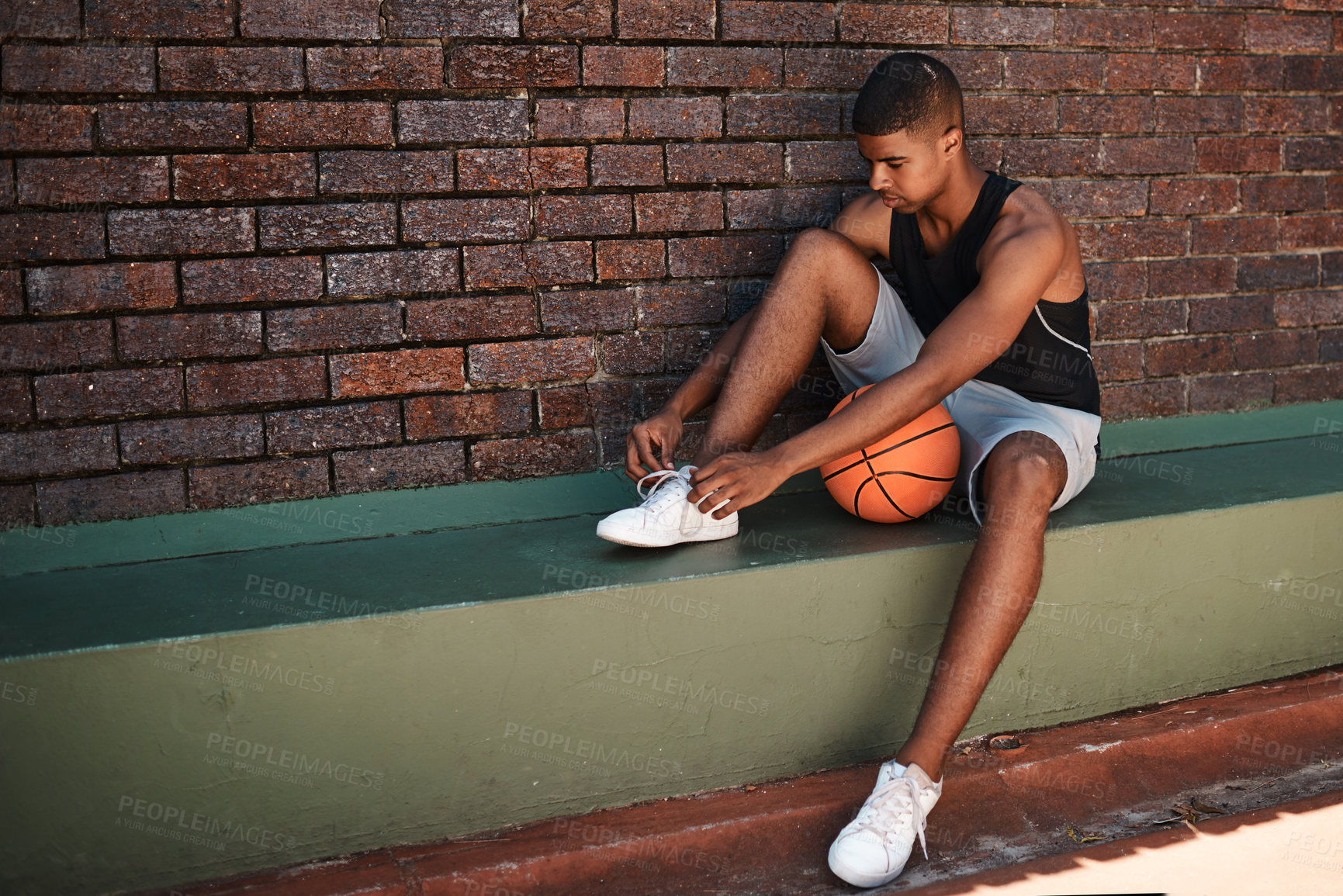 Buy stock photo Shot of a sporty young man tying his laces while playing basketball outdoors