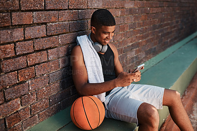 Buy stock photo Shot of a sporty young man using a cellphone while taking a break after a game of basketball