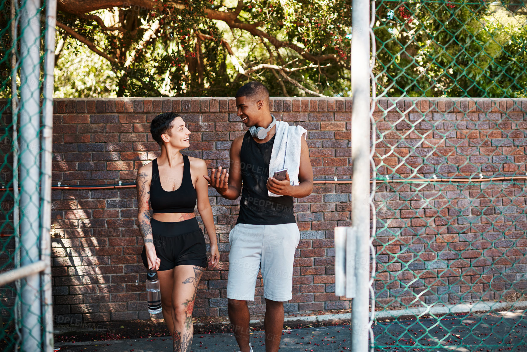 Buy stock photo Shot of two sporty young people chatting to each other while walking into a sports court