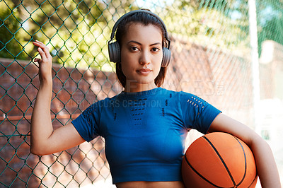 Buy stock photo Portrait of a sporty young woman holding a basketball while standing against a fence outdoors