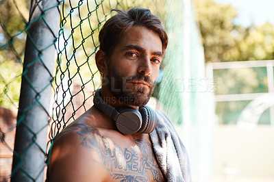 Buy stock photo Portrait of a sporty young man taking a break while standing against a fence outdoors