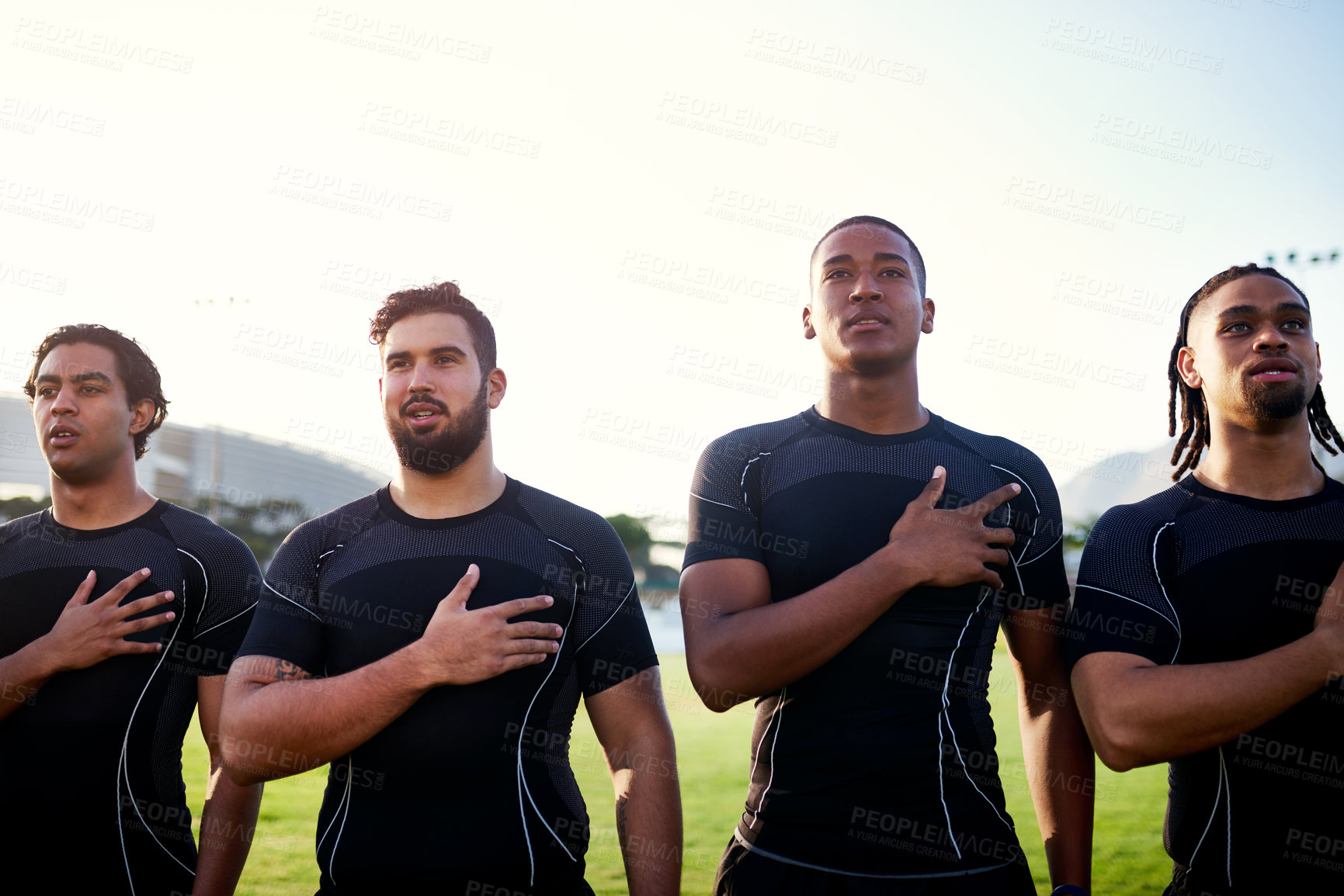 Buy stock photo Cropped shot of a diverse group of sportsmen standing together and singing their national anthem before playing rugby