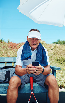 Buy stock photo Cropped shot of a handsome mature sportsman sitting alone and using his cellphone after playing tennis