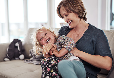 Buy stock photo Cropped shot of an attractive young mother sitting and tickling her daughter during a day at home