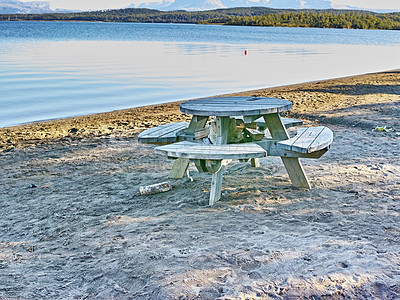 Buy stock photo Wooden picnic bench and table at a lake with calm waters and sandy shore in Bodo Nordland Norway. Seating at a scenic reservoir to enjoy a peaceful break along the coast while traveling and exploring