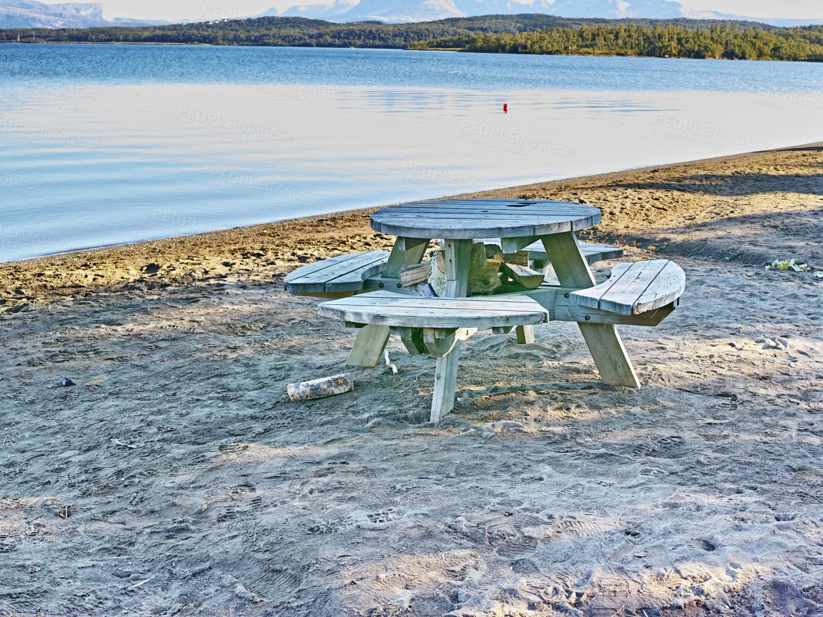 Buy stock photo Wooden picnic bench and table at a lake with calm waters and sandy shore in Bodo Nordland Norway. Seating at a scenic reservoir to enjoy a peaceful break along the coast while traveling and exploring