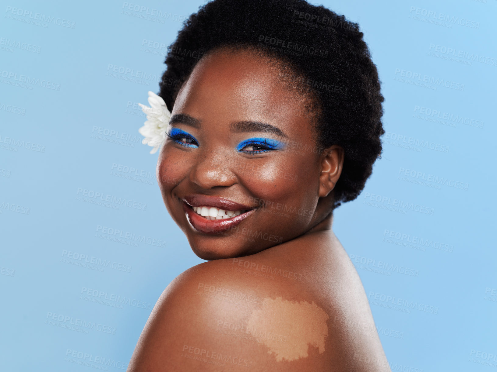 Buy stock photo Studio shot of a beautiful young woman with a flower behind her ear against a blue background
