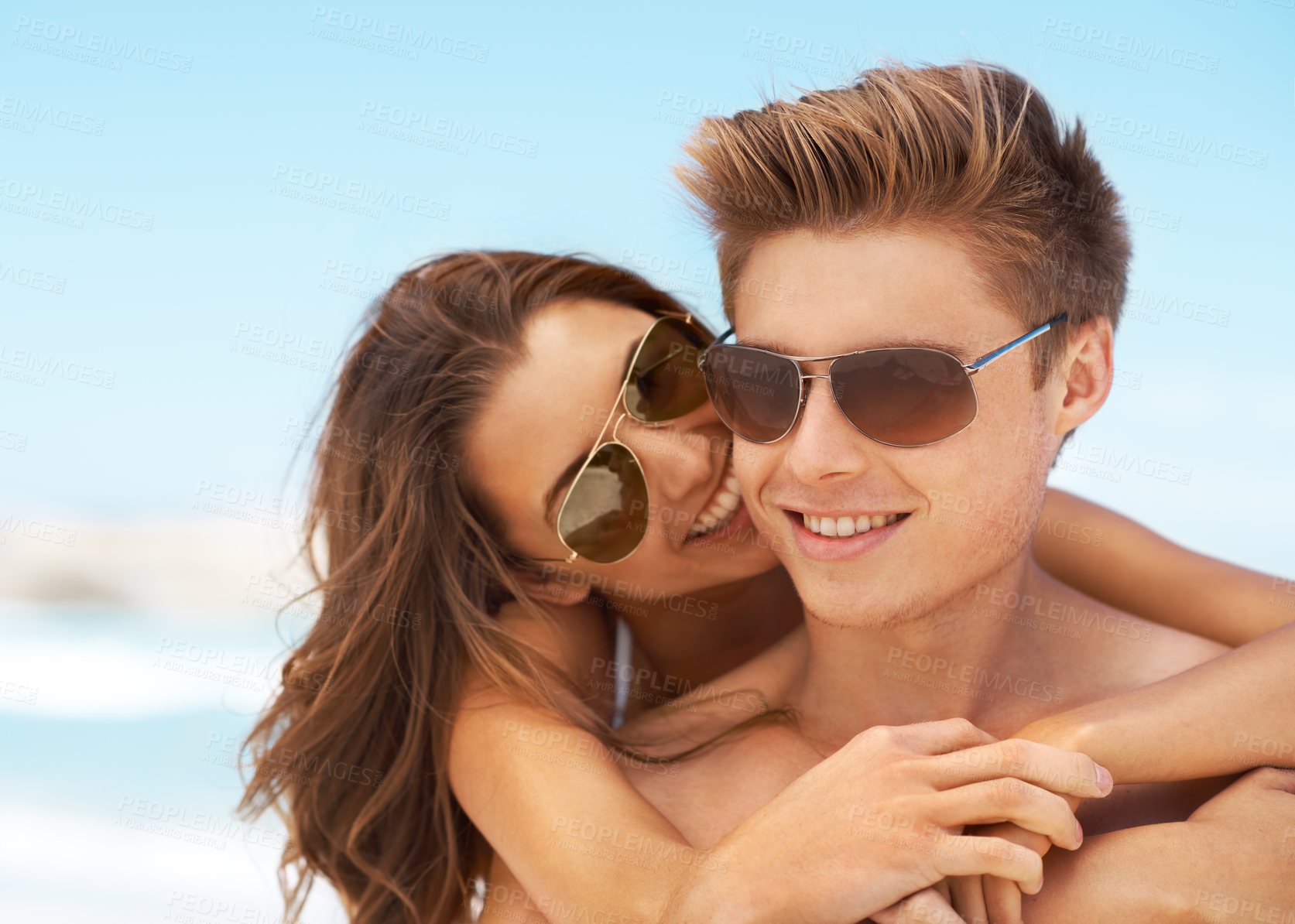 Buy stock photo Cropped shot of an affectionate young woman embracing her boyfriend while standing at the beach during the day