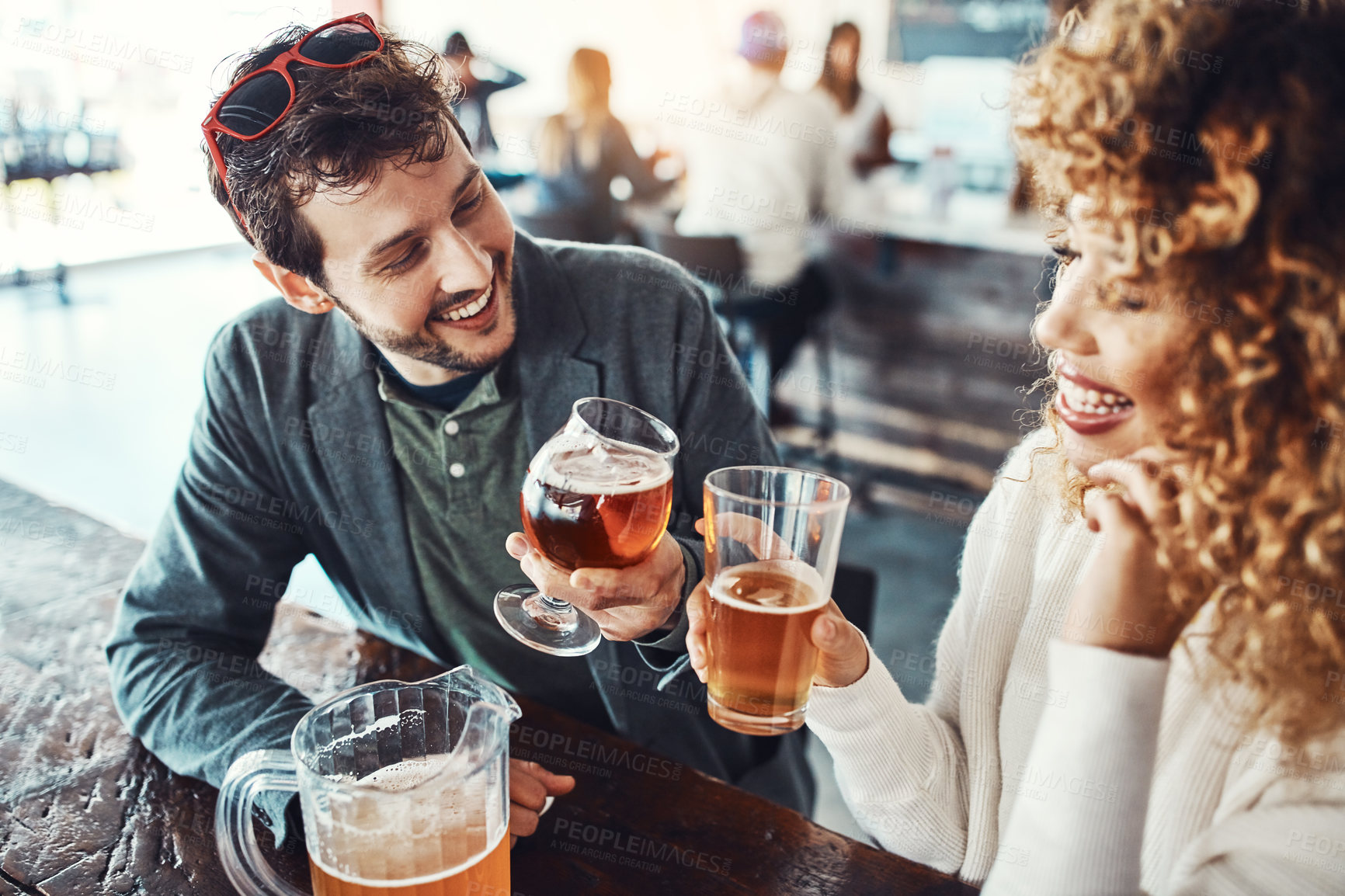 Buy stock photo Shot of a happy young man and woman toasting with beers at a bar
