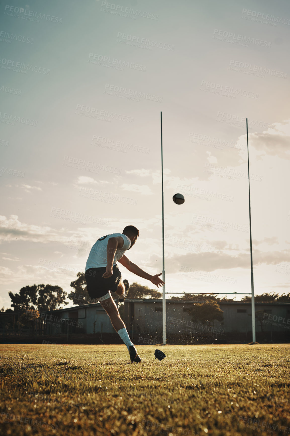 Buy stock photo Full length shot of a handsome young rugby player kicking a ball on the field during the day