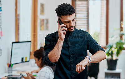 Buy stock photo Shot of a young businessman using a smartphone and checking the time in a modern office