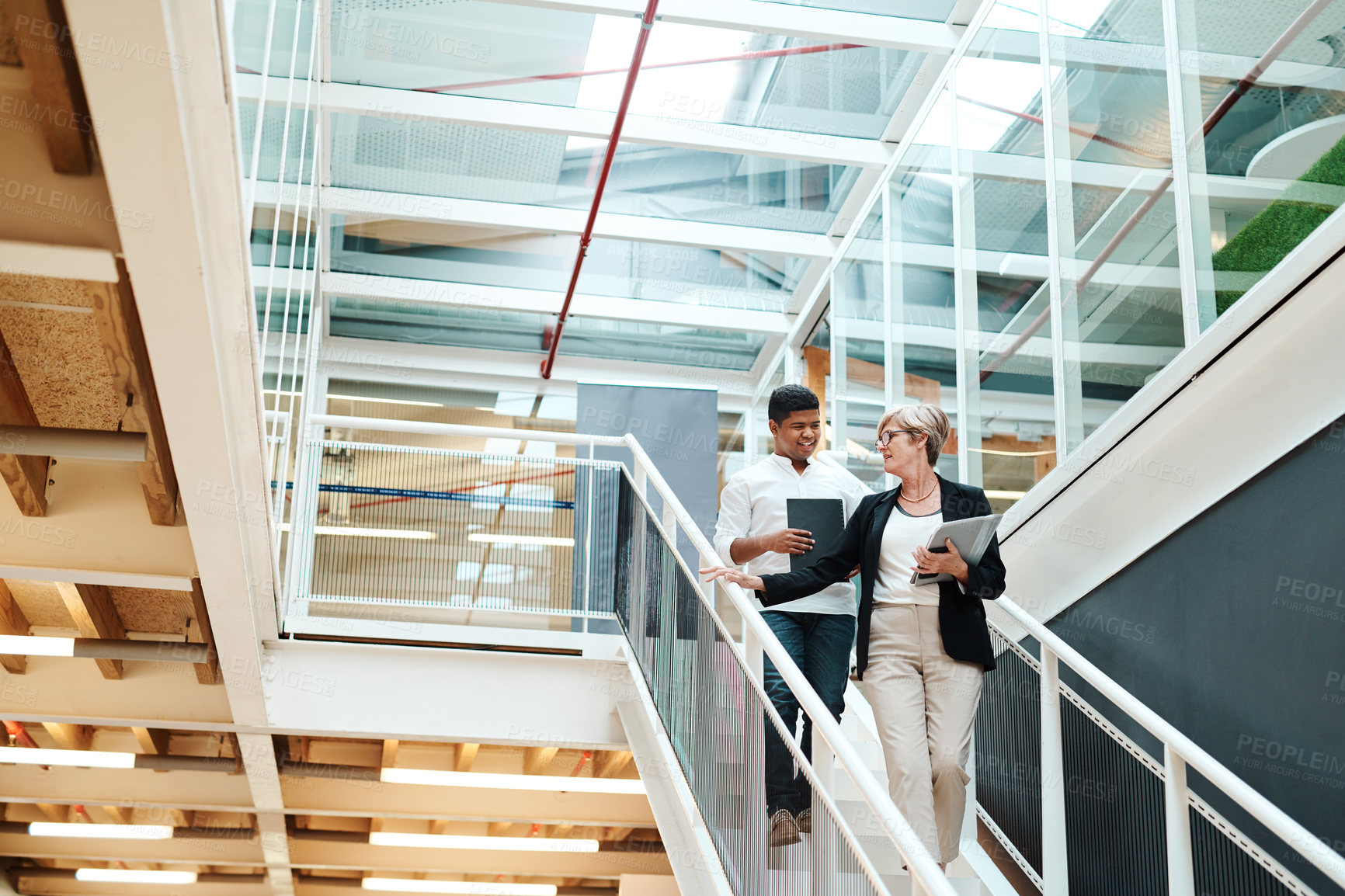 Buy stock photo Shot of two businesspeople walking down a staircase together in an office