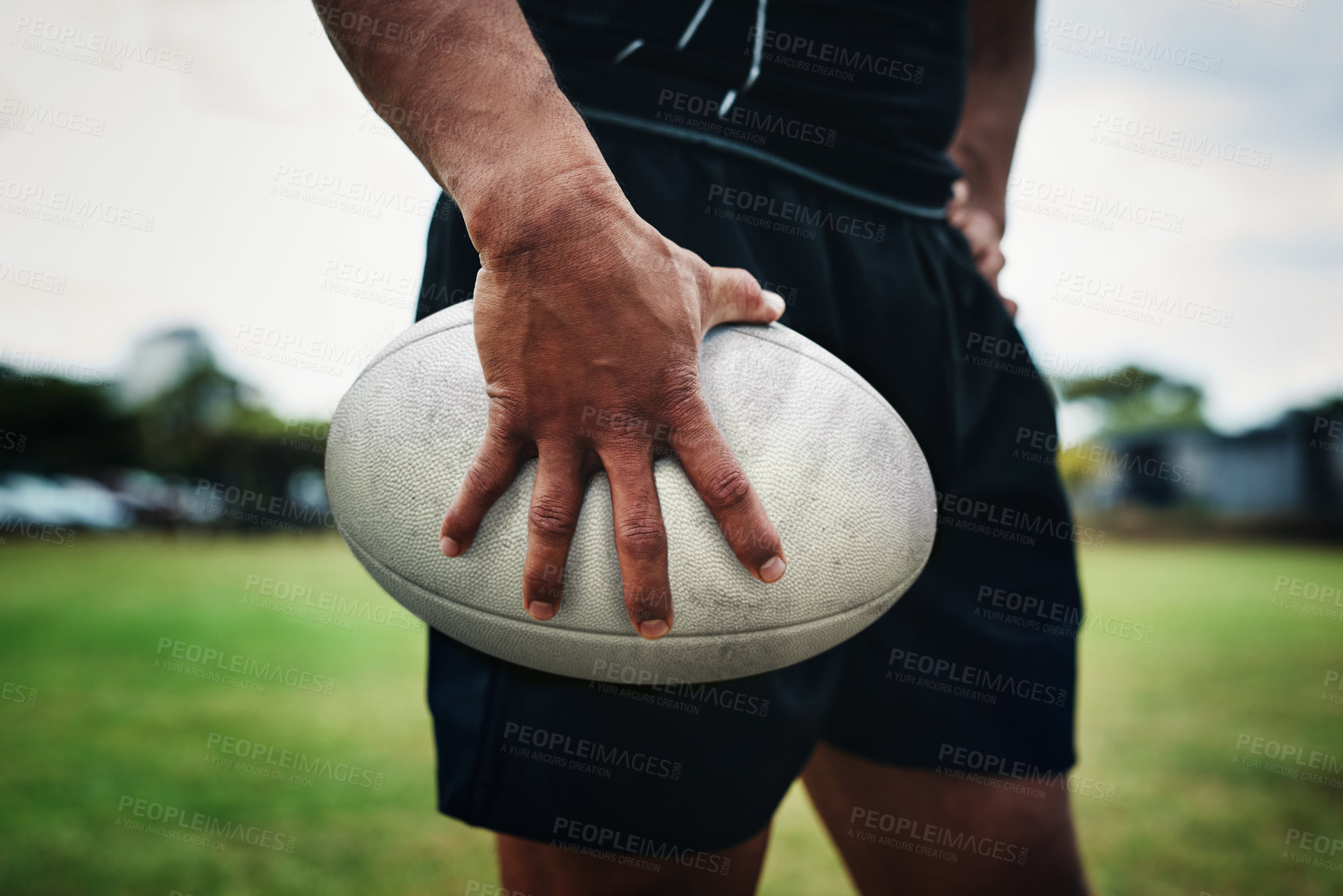 Buy stock photo Cropped shot of an unrecognizable rugby player holding a rugby ball on the field during the day