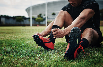 Buy stock photo Cropped shot of an unrecognizable rugby player tying his shoelaces while sitting on the field during the day