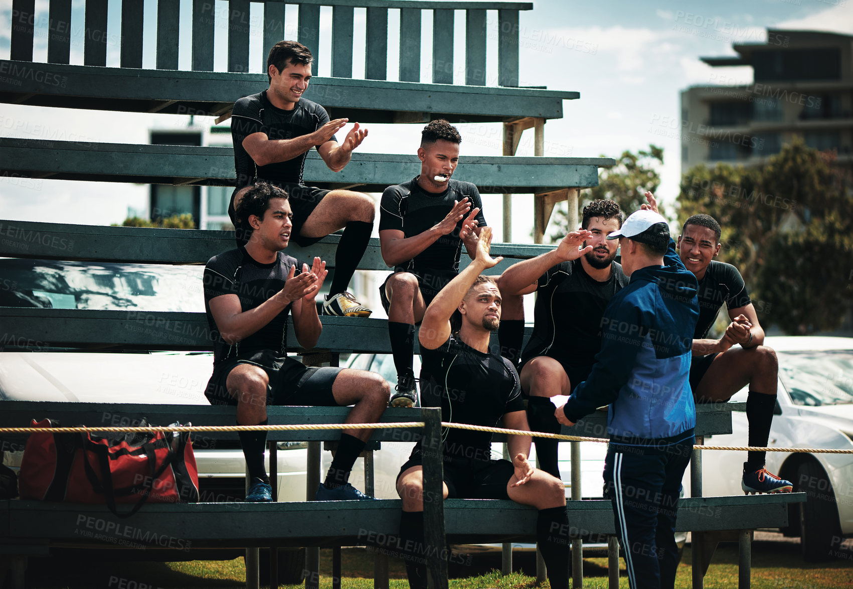 Buy stock photo Cropped shot of a team of rugby players clapping for their coach while sitting on the bench near the field