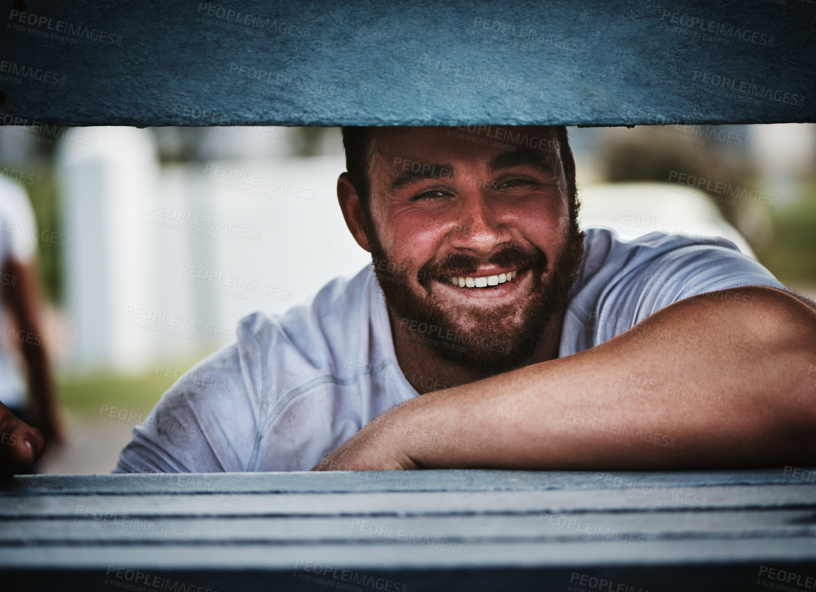 Buy stock photo Cropped portrait of a handsome young rugby player smiling while sitting on the bench near the field