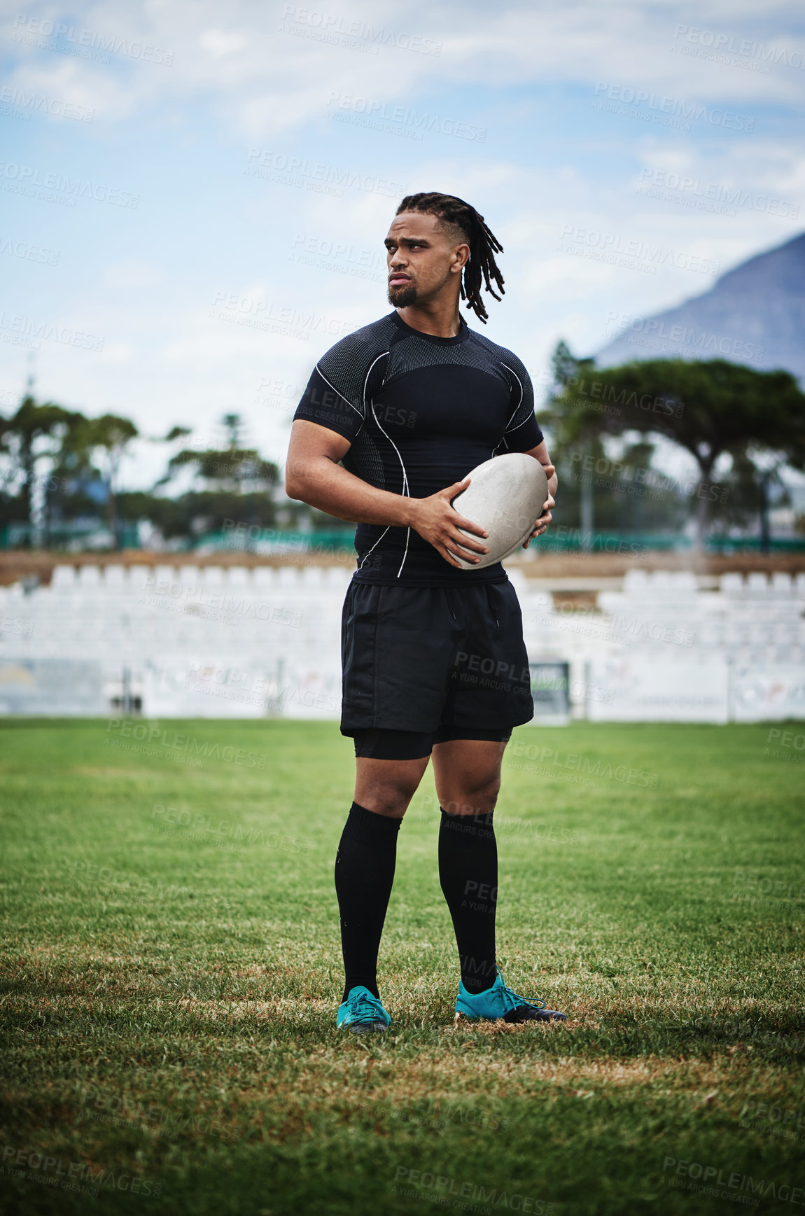 Buy stock photo Full length shot of a handsome young rugby player holding a rugby ball while standing on the field